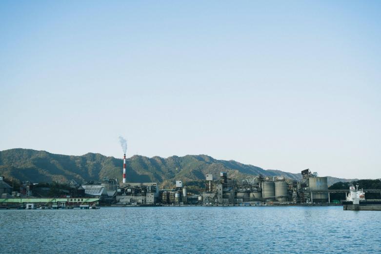 <span style="font-size:12px;"><font color="ffffff"> セメント町はセメント工場の門前町とも言われており、まちの北には多くの工場が立ち並びます。<br> <br> 東九州の主要都市を経由する日豊本線が開業し、1916年に臼杵駅・佐伯駅間が開通すると、翌年からセメント生産が相次いで開始され、まちの中心産業となっていきます。また、リアス海岸である津久見港は水深がとても深いため、６万トンクラスの大型船が接岸して、一度に多くの石灰石やセメントを運ぶことができます。<br> <br> 鉱山から工場、そして出荷するための港までの距離がとても近いため、津久見は「日本一の石灰石のまち」となったのです。その生産量は年間約2500万トンといわれ、現在でも国内有数の量を誇っています。</font></span><br><br>