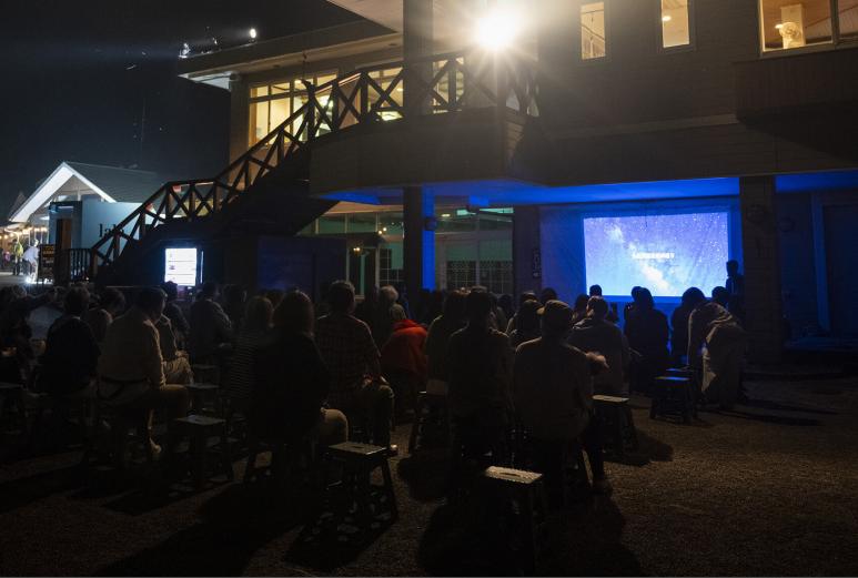 <span style="font-size:12px;"> 19時から「星のお話し」がスタートします。<br> <br> 19時になると、いよいよお待ちかねのプログラムがスタート！ まずはプロジェクターを使った「星のお話し」から。夜空に瞬く星たちの正体や、星座にまつわるギリシャ神話、宇宙のふしぎなどを、やさしく、そしてワクワクするように解説してくれます。まるで物語の世界へ入り込んだようなひとときに、大人も子どもも夢中に。常連の家族連れも多く、小さな子どもたちが目を輝かせながら星の話を聞く姿は、見ているだけで心があたたかくなります。<br> <br> そしてもうひとつのお楽しみが、園内に設けられた「天体望遠鏡コーナー」。自由に参加できるので、気軽にのぞいてみると――そこには、クレーターまでくっきり見える月や、遠く輝く惑星たちの姿が！ 思わず「わあ！」と声が漏れるほどの感動に、宇宙の大きさを肌で感じられる体験です。</span><br><br>