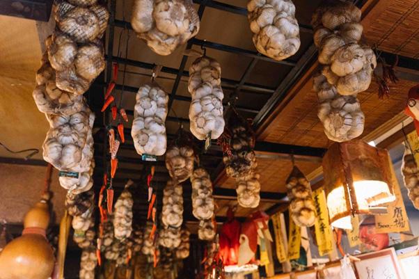 <span style="font-size:12px;">店内の天井には、料理に欠かせないにんにくが大量に吊るされていました。壁には著名人が来店した写真が収まりきらないほど飾られていて、有名店ならではの活気に満ちています。<br> <br> 開店すると続々とお客さんが入り、ママさんは厨房からオーダーを聞き、何人前もの料理を捌いていきます。山下さんは予約電話を取りながら、馴染みのお客さん全員に声をかけて話に花を咲かせます。<br> <br> 「お客さんが『もうちょっと辛いのが好きやな』と席で会話しているのを耳にしたら僕が出てきて、『辛いの好きですか？』と辛いタレをすぐ出す。すると『わ〜うめ〜！』と感激してくれる。そういう風にお客様の様子を見ながらキャッチする。それが我々の仕事です」<br> <br> 山下さんの好きな言葉は「味一筋に信念を貫く」。<br> <br> 「基本は滋養食。うちの料理を食べたらみんなが健康で元気になってほしい。そういう願いで料理をつくっています」と語る山下さんの料理は、多彩な経験から生まれた体にやさしく温まるものばかりでした。</span>