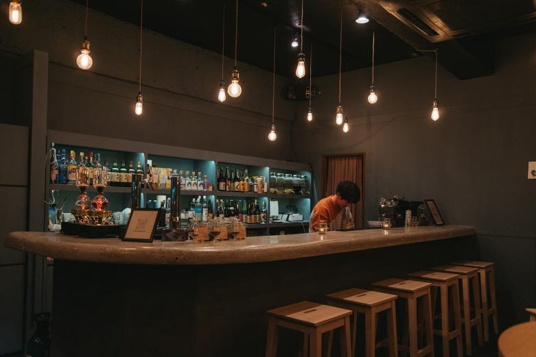 <span style="font-size:12px;"><font color="ffffff"> ペンダントライトで幻想的な雰囲気を演出。<br> <br> 巡同様、この店も〈丸田酒舗〉による経営。2代目・丸田晋也さんは「酒好きだけが通うバーにしてしまうよりも、もっと気軽に使ってもらえるような店にしたかったんです。カフェと思ってやってきたお客様が、コーヒーを飲む感覚で良質な蒸留酒に触れる。そういうきっかけがつくれればうれしいですね」と教えてくれました。</font></span><br><br>