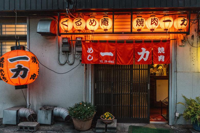 <span style="font-size:12px;">まず紹介したい一軒目は、別府市駅前本町にある〈焼肉ホルモン 一力（いちりき）〉。<br><br>創業から50年、半世紀続く人気の焼肉店です。<br><br>17時、そっと扉を開けていざ入店。<br>蛍光灯に照らされたカウンターにガスロースターが並び、テキパキと準備する店員さんたちで活気に満ちた空間が出迎えてくれます。<br><br>編集者コメント： 「出張で別府に来るたびに気になっていた赤提灯の一力さん。ちょっと勇気を出して暖簾をくぐってみたら、期待通りの味のあるいい雰囲気。カウンターで隣になった地元のおじさんに『ぜひ食っていけ』と言われたのがシン刺し。もちろん焼肉も絶品です！」（編集者A）</span><br><br>