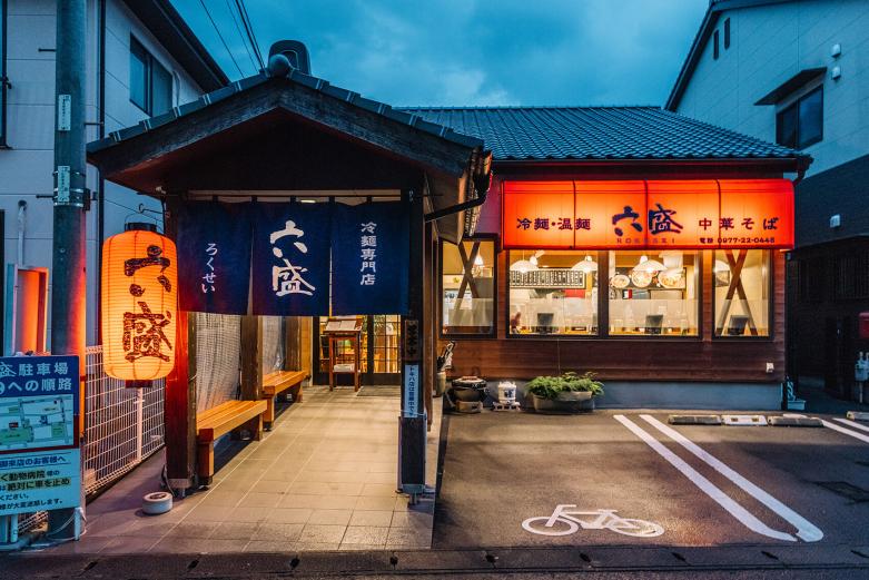 <span style="font-size:12px;">本日３軒目、最後にご紹介するのは〈手のべ冷麺専門店　六盛〉です。<br> <br> 編集者のコメント： 別府グルメと言えば、別府冷麺もそのひとつですが、有名店ながらオススメなのは〈六盛〉。しかし、ここでは通ぶって「中華そば」をオススメしたい。醤油ベースのシンプルな一品。黄金色のスープは上品な口当たりで、細麺も丁寧な仕事ぶりが伺えます。シメの一杯にどうぞ。（編集者A）<br> <br> ３店舗あるうちの松原本店を訪れました。<br> <br> 別府市内では「別府冷麺」の看板をよく見かけますが、そもそも別府冷麺のルーツは、昭和25年頃、当時満洲に住んでいた日本人が引き揚げて来て開いたお店が始まりなのだとか。<br> <br> 六盛は、創業者である関屋さんご夫婦が日常で食べていた別府冷麺の味が忘れられず、「あのお店のようにおいしい冷麺を自分たちの手でつくってみよう」と冷麺づくりを始め、当時の酒屋をやっていた場所で2001年に六盛をオープン。それから23年、昔ながらの別府冷麺の味の研究を追求し続けてきました。冷麺だけでなく、温麺や中華そば、とんこつラーメンなどを出す実力派の人気店です。</span><br><br>