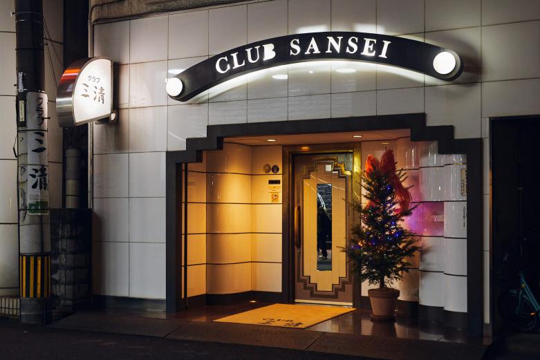 <span style="font-size:12px;"><font color="ffffff">淳子ママいわく、「着物は日本人のナショナルユニフォーム」。この日も上品な色香を放つ和装で取材陣を出迎えてくれました。<br> <br> 店は約50坪。創業当時から変わらぬゴージャスなシャンデリア、貴重な一枚板の壁、手彫りの欄間（らんま）、レトロなランプなどでオーセンティックに彩られ、中央のグランドピアノも存在感を放っています。</font></span><br><br>