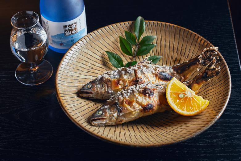<span style="font-size:12px;"><font color="ffffff">「鮎の塩焼き」990円。三隈川のきれいな水で育まれる鮎は大きく、肉厚でジューシーな身がたっぷり。同じく日田にある蔵元、井上酒造が醸す、吟醸酒〈寒山水仙〉とともに味わって日田づくしの夜を。</font></span>
