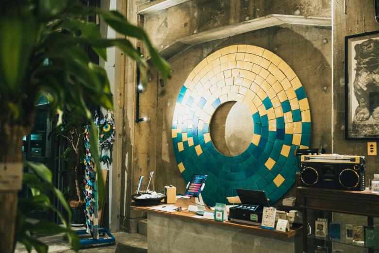 <span style="font-size:12px;"><font color="ffffff"> 坂本和歌子さんの作品『はじまり』。<br> <br> まず入ってすぐ、チェックインデスクの背後にある大きな作品に目を奪われます。これは、HAJIMARI Beppuの宿主でもある陶芸家、坂本和歌子さんの作品。海から太陽が昇るイメージを陶器で表現したウォールアートです。坂本さんはこの場所でサテライトアトリエと焼き菓子のショップ〈うみとじかん〉も運営し、坂本さんのすてきな器も購入することができます。</font></span><br><br>